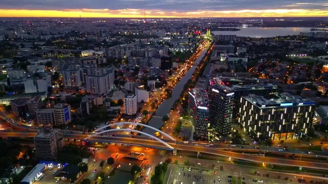 Drone aerial footage of a spectacular sunset in Bucharest, Romania. The camera captures the scenic Dambovita River in the Orhideea business area, showcasing modern office buildings, vibrant golden hou
