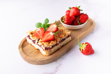 Sweet homemade pie with strawberry jam, decorated with fresh strawberries and aromatic herbs on the wooden tray on white marble table close up. © Iryna