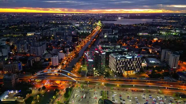 Drone aerial footage of a spectacular sunset in Bucharest, Romania. The camera captures the scenic Dambovita River in the Orhideea business area, showcasing modern office buildings, vibrant golden hou