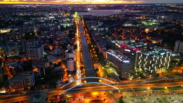 Drone aerial footage of a spectacular sunset in Bucharest, Romania. The camera captures the scenic Dambovita River in the Orhideea business area, showcasing modern office buildings, vibrant golden hou