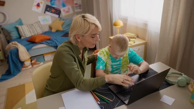 High angle shot of Caucasian mother and Caucasian boy with Down syndrome using laptop computer for online learning. Clip perfect for inclusive education and special needs support campaigns