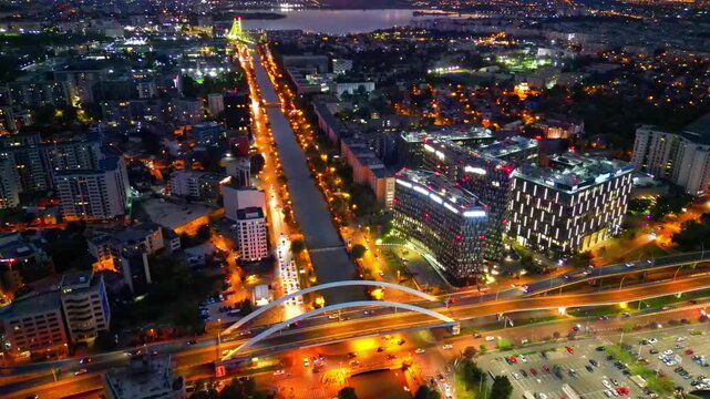 Drone aerial footage of a spectacular sunset in Bucharest, Romania. The camera captures the scenic Dambovita River in the Orhideea business area, showcasing modern office buildings, vibrant golden hou