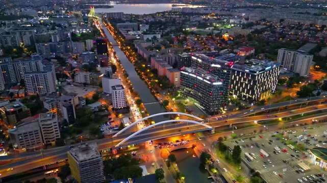 Drone aerial footage of a spectacular sunset in Bucharest, Romania. The camera captures the scenic Dambovita River in the Orhideea business area, showcasing modern office buildings, vibrant golden hou