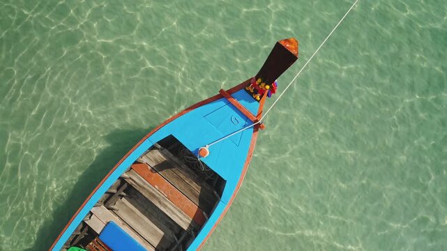 Close up traditional longtail boat floating on clear turquoise water next to a tropical beach, ready for island hopping and exploring the beautiful coastline of Thailand. Aerial top down drone shot