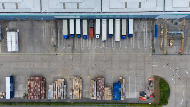 Aerial view of Kettering industrial Warehouses showing loading docks with parked semi-trucks and rows of wooden pallets stored in the yard in Kettering, England, United Kingdom.