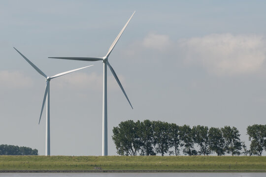 Breskens, Netherlands. Onshore wind turbines along the Westerschelde dike with trees and estuary landscape representing renewable energy infrastructure