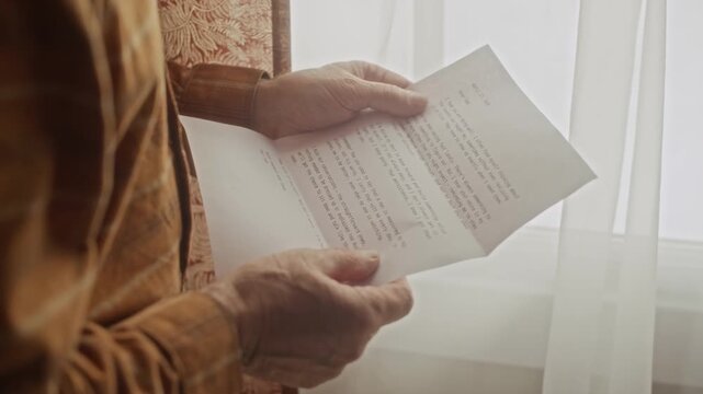 Cropped shot of senior man standing near window, opening paper envelope and reading letter. Clip is suitable for marketing campaigns focusing on retirement, pension plans, or elderly loneliness