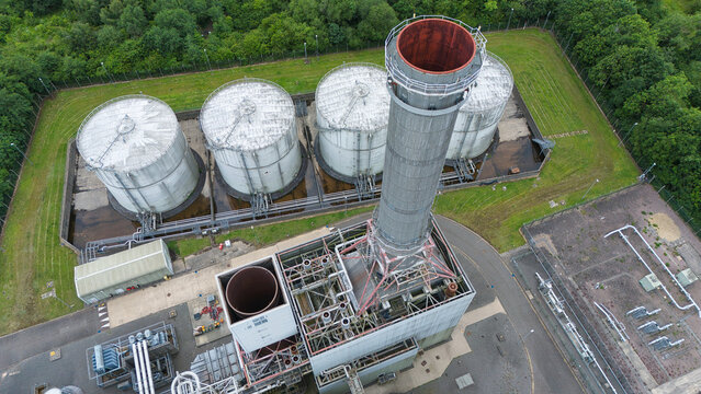 Aerial view of Corby Power Station showing the tall chimney stack, large industrial storage tanks, and surrounding green trees in Corby, England, United Kingdom.