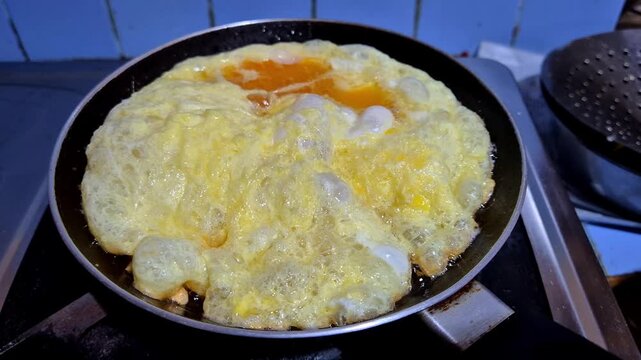 Horizontal high angle close up shot of a fluffy telur dadar or omelet bubbling and frying in hot oil inside a non-stick pan on a kitchen stove. An omelet being cooked in a frying pan