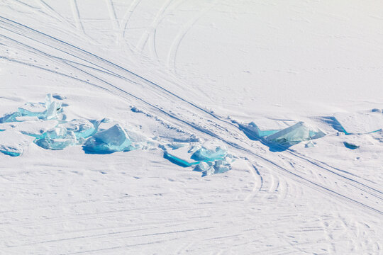 Aerial view of frozen Lake Baikal with turquoise ice chunks and snowmobile tracks on the snow-covered surface in Baikal'skoe, Buryatia, Russia.