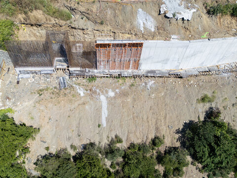 Aerial view of a construction site featuring a reinforced concrete retaining wall, exposed rebar structures, and earthworks in a hillside area in Istanbul, Istanbul, Turkiye.