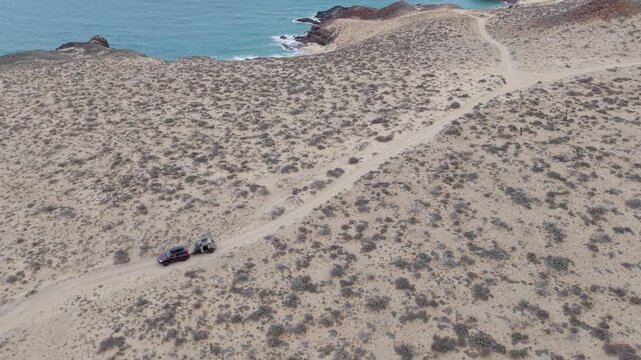 Suv tows a teardrop camper trailer over sandy terrain on an overland trail in Baja California, Mexico.