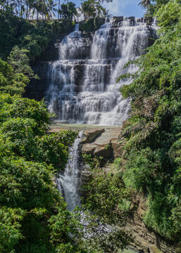 Aerial view of the multi-tiered Cigangsa Waterfall cascading over rocky cliffs surrounded by lush tropical vegetation, West Java, Indonesia.
