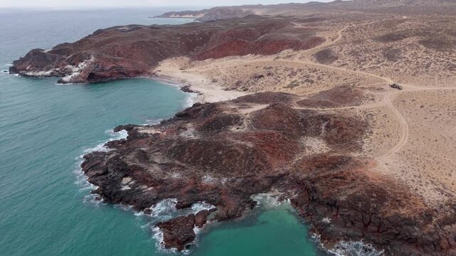 Suv and teardrop camper trailer are parked on a cliff overlooking the Pacific Ocean during an overland adventure in Baja California.