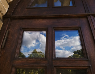Fototapeta premium Clean windows of a aged history design wooden old doors closed church, temple with blue sky reflections in the glasses. Day sun clear light. Concept of spiritual growth, mind. Different angles