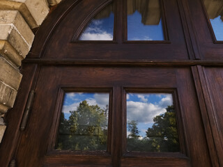 Fototapeta premium Clean windows of a aged history design wooden old doors closed church, temple with blue sky reflections in the glasses. Day sun clear light. Concept of spiritual growth, mind. Different angles