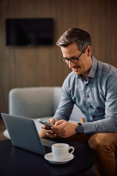Smiling businessman texting on mobile phone while working in office.