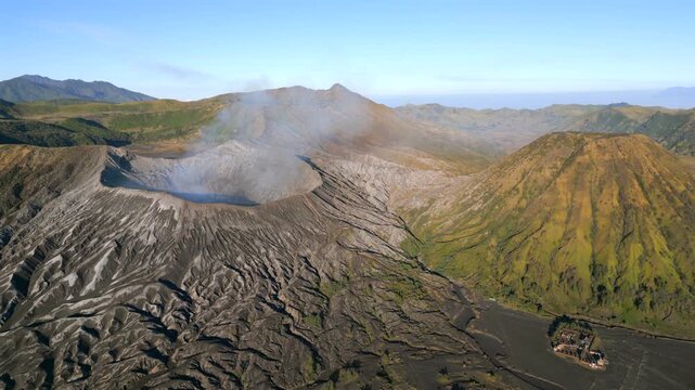 Aerial view of Mount Bromo volcano with a steaming crater and Mount Batok rising beside it at sunrise. Dramatic volcanic landscape in East Java, Indonesia.