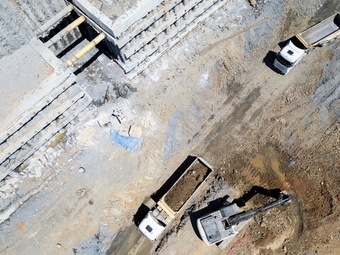 Aerial view of a construction site with heavy machinery including dump trucks and an excavator working near concrete foundation structures in Istanbul, Istanbul, Turkiye.