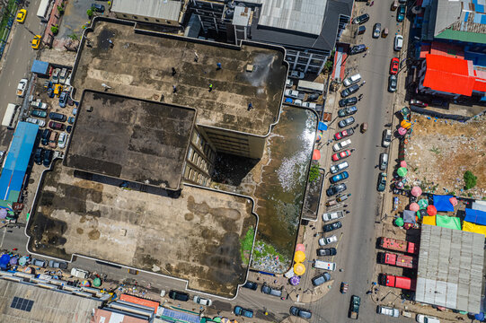 Aerial view of a large commercial building with a flat roof, surrounded by busy streets, parked cars, and vibrant market stalls in Monrovia, Montserrado, Liberia.