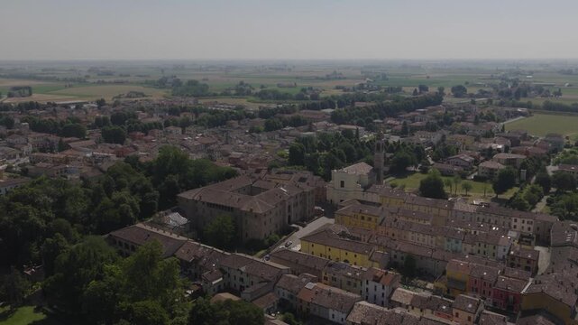 Aerial drone view of Soragna, Italy, featuring the historic fortress and adjacent church, surrounded by charming town architecture and green landscape in soft daylight.