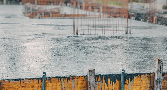 Wet concrete foundation slab with formwork and steel reinforcement mesh on a building construction site