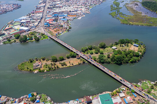 Aerial view of a bridge connecting urban districts over the Mesurado River with dense buildings and lush green islands in Monrovia, Montserrado, Liberia.