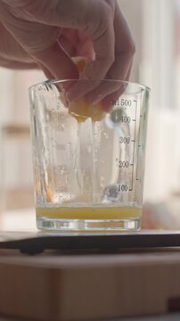 Hand squeezes orange juice into glass measuring cup. Concept of fresh citrus juice and food preparation