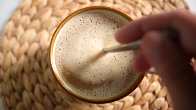 A top view of a mug of cappuccino being stirred with a spoon