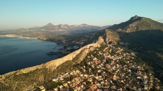 Stunning aerial panorama capturing a vibrant Mediterranean town nestled against rugged hills, stretching towards the shimmering coastline under the golden glow of sunrise. Calpe, Costa Blanca, Spain