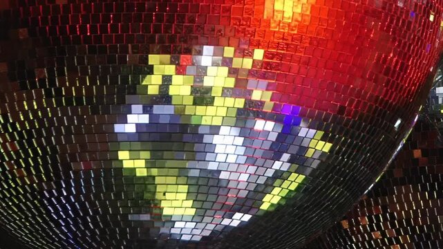 A dazzling disco ball gleams under dynamic party lights, showcasing brilliant shifts from fiery red to cool blue-green and vibrant purple.