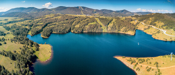 Zlatibor Ribnica Lake with deep blue water nestled among green hills and pine forests, featuring a long gondola moving above © EdNurg
