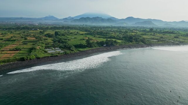 Aerial patchwork rice fields and coastal ponds meeting rocky shore drone mapping shot highlighting irrigation grids, wet paddies, farm tracks and distant volcanic ridge,Bali island