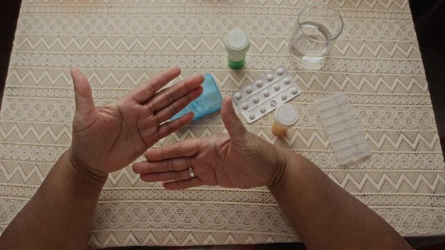 Overhead of senior African American woman opening hands at table with medicine organizer and water. Clip is perfect for senior healthcare, pharmaceutical marketing, and geriatric care campaigns