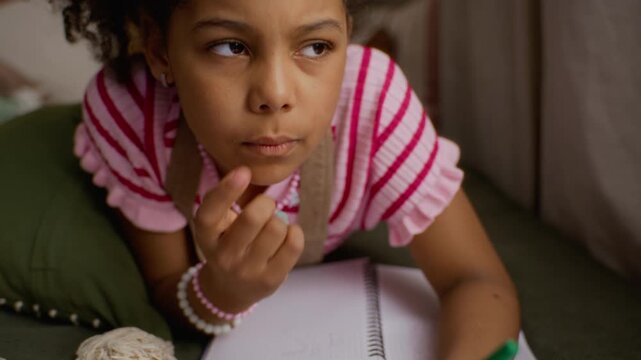African American child writing on school worksheet with pen, pausing to think thoughtfully while looking away. Video perfect for elementary education, homeschooling, and learning concepts