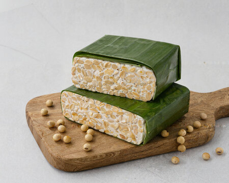 Fresh organic tempeh blocks wrapped in green banana leaf with soybeans