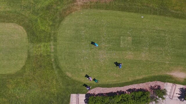 Top-down aerial shot of golfers on a fairway at Warm Springs Golf Course, Boise, Idaho. One player has just teed off with visible club motion and shadows on a sunny spring day.