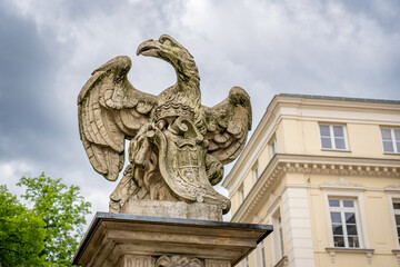 Fototapeta premium Stone eagle sculpture in Warsaw square on ornate pedestal, historic building, overcast spring sky