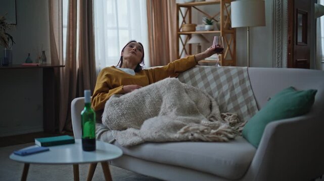 Thoughtful lady holding goblet sitting quietly sofa home covered blanket