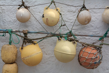 Vintage marine buoys and fishing floats hanging on ropes against a white textured wall in Agaete, Gran Canaria, Spain. © Javier