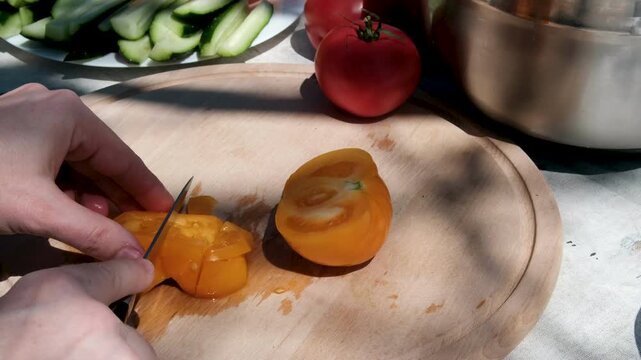 Fresh cucumbers and tomatoes from a home garden are being chopped on a wooden table outdoors in a rural village creating a healthy homemade salad . sunny natural countryside setting.