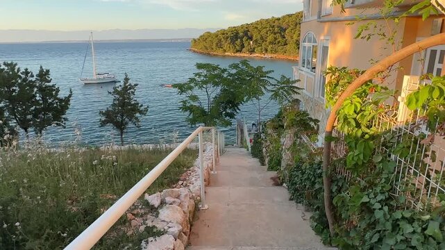 Walking down the stairs to the water at a coastal location with a sailboat in the distance during sunset