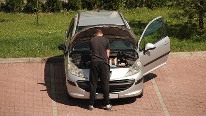 Mężczyzna stoi przed samochodem z otwartą maską na parkingu i sprawdza silnik. © tomo81