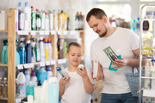 Buyers picked up oral care products. Dad and son took toothpaste, toothbrush, and mouthwash from shelf of showcase and are looking for additional remedy for gum health.
