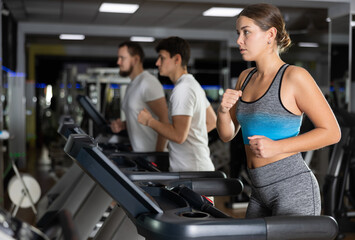 Fototapeta premium In gym, girl does exercises using treadmill. Young group of athletes trains in gym. Physical education and sports, active healthy lifestyle.