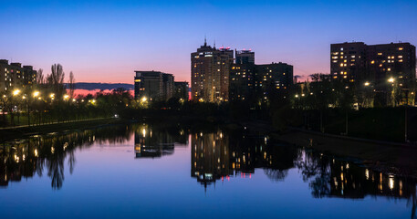 Obraz premium City skyline reflecting in calm lake water at dusk with vibrant blue and pink twilight sky