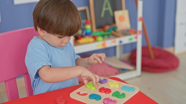 Boy placing colorful wooden number puzzle pieces with right hand at red table in building; learning concentration.