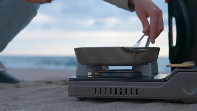 Cooking halloumi cheese on portable stove at beach. Halloumi cheese sizzling on portable gas stove, golden sandy beach stretching toward blue sea horizon, creating scenic outdoor