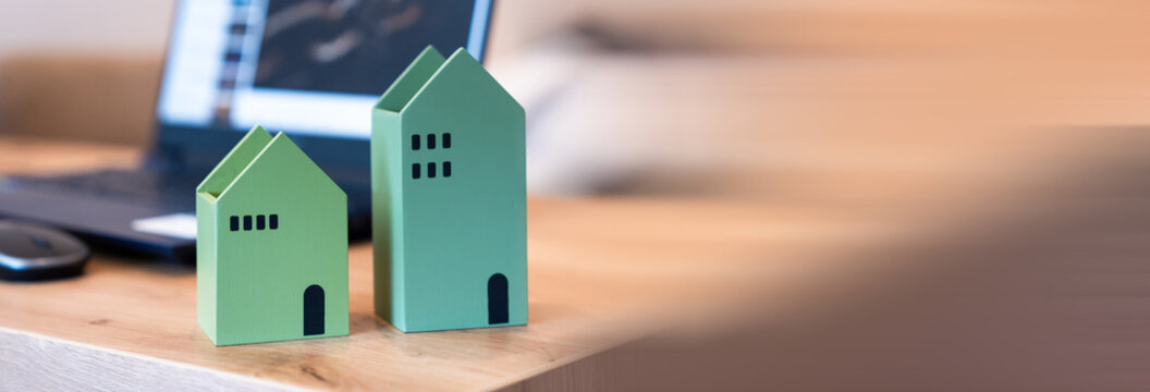 Paper house models on office desk with documents and calculator representing real estate business, property investment, and decision to buy or sell an apartment.