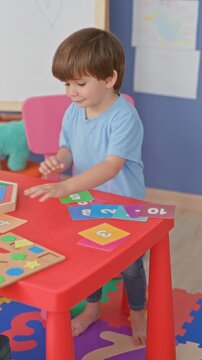 Boy standing at red play table placing colorful number cards with bare hand in studio; concentration learning.